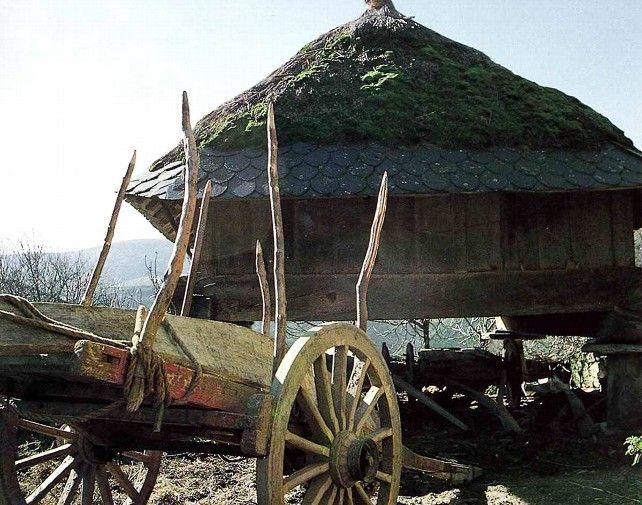 Un carro y un hórreo fotografiados en un pueblo leonés en el siglo XX.
